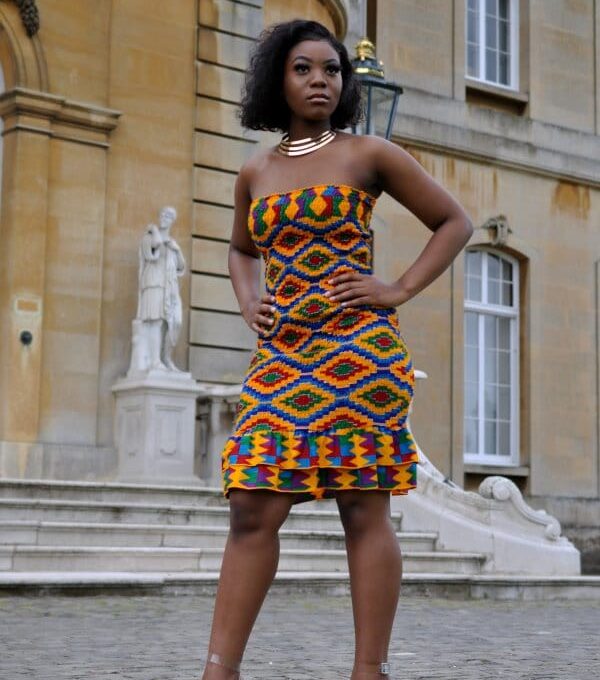 Frontal of model wearing a colourful strapless bodycon dress with all over African Kente print pattern and layered ruffle hem.