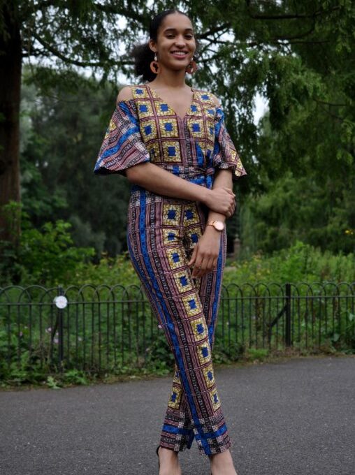 Frontal of model wearing a blue and gold African Ankara print jumpsuit with cold shoulder and butterfly sleeves.