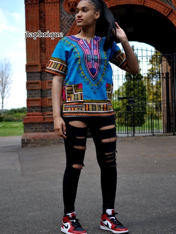 Full frontal of model wearing a ladies light blue and traditional African Dashiki shirt with pink and multi-coloured Angelina pattern on chest, sleeves and hem.