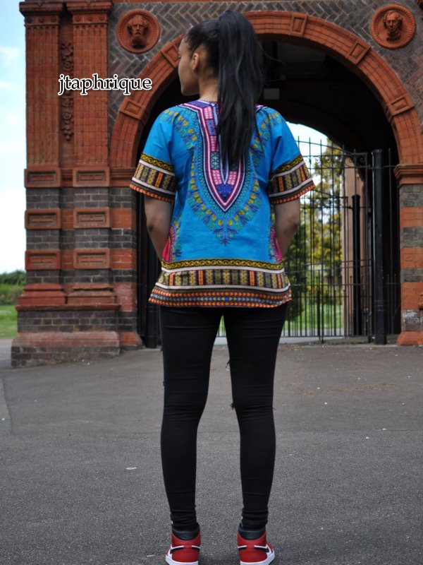 Back shot of model wearing a ladies light blue and traditional African Dashiki shirt with pink and multi-coloured Angelina pattern on chest, sleeves and hem.