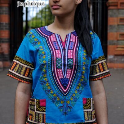 Close front shot of model wearing a ladies light blue and traditional African Dashiki shirt with pink and multi-coloured Angelina pattern on chest, sleeves and hem.