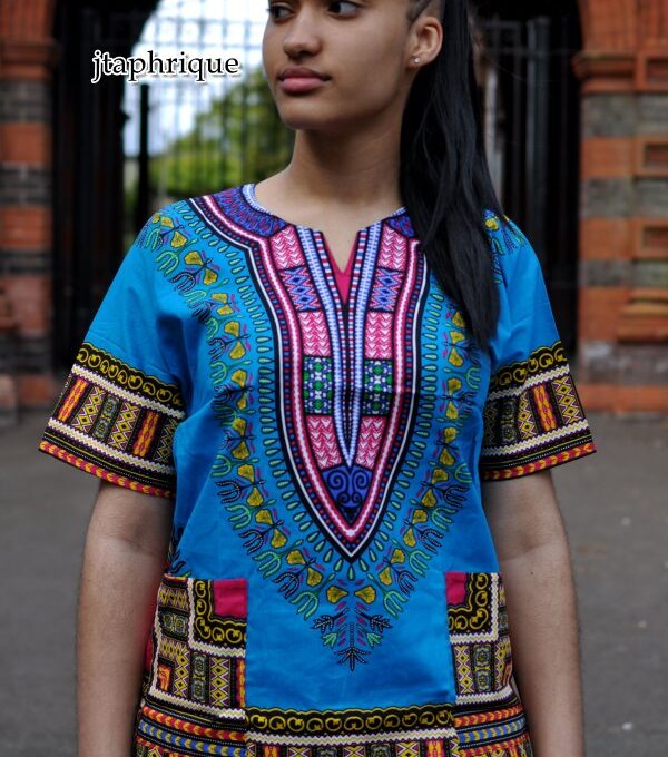 Close front shot of model wearing a ladies light blue and traditional African Dashiki shirt with pink and multi-coloured Angelina pattern on chest, sleeves and hem.