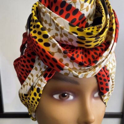 Close front shot of mannequin wearing a pre-tied colourful head wrap or turban in all over re, yellow, white and gold African print.