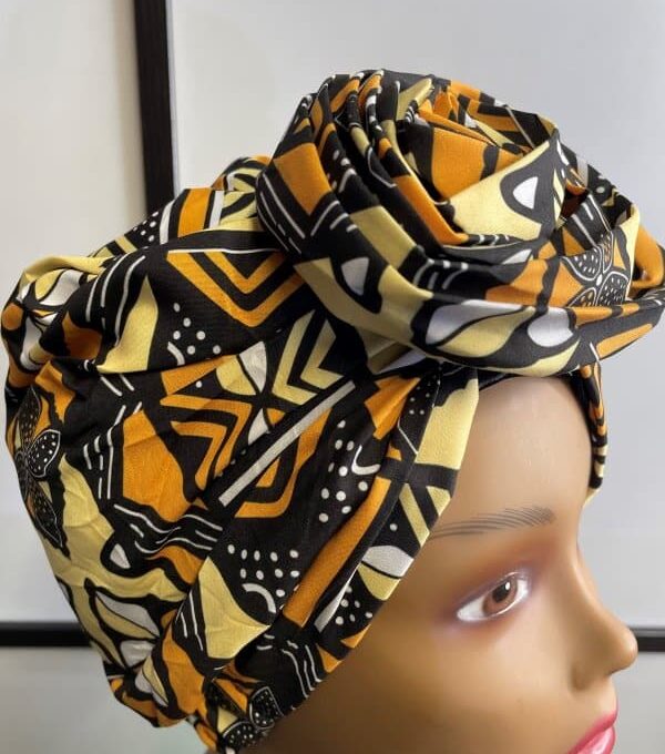 Close shot of mannequin wearing a pre-tied head wrap or turban in all over yellow and multi-coloured African print.