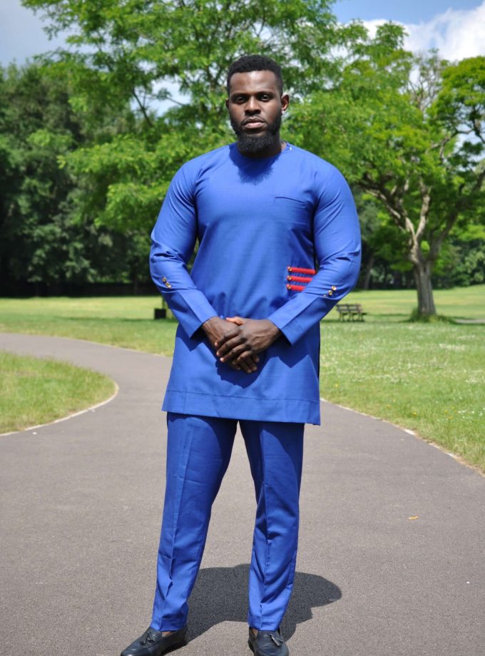 Full frontal of model wearing a solid blue African men's suit with a red 3 stripe pattern and buttons on left front side.
