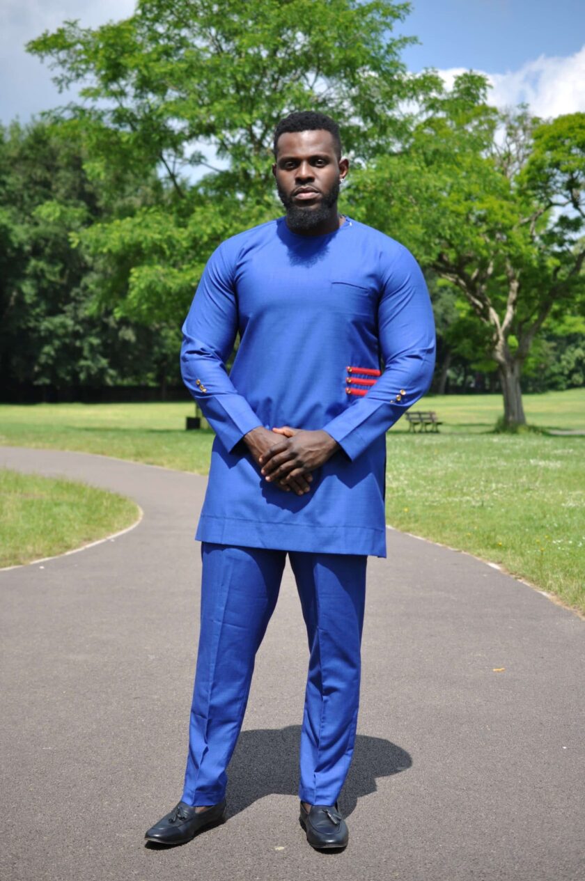 Full frontal of model wearing a solid blue African men's suit with a red 3 stripe pattern and buttons on left front side.