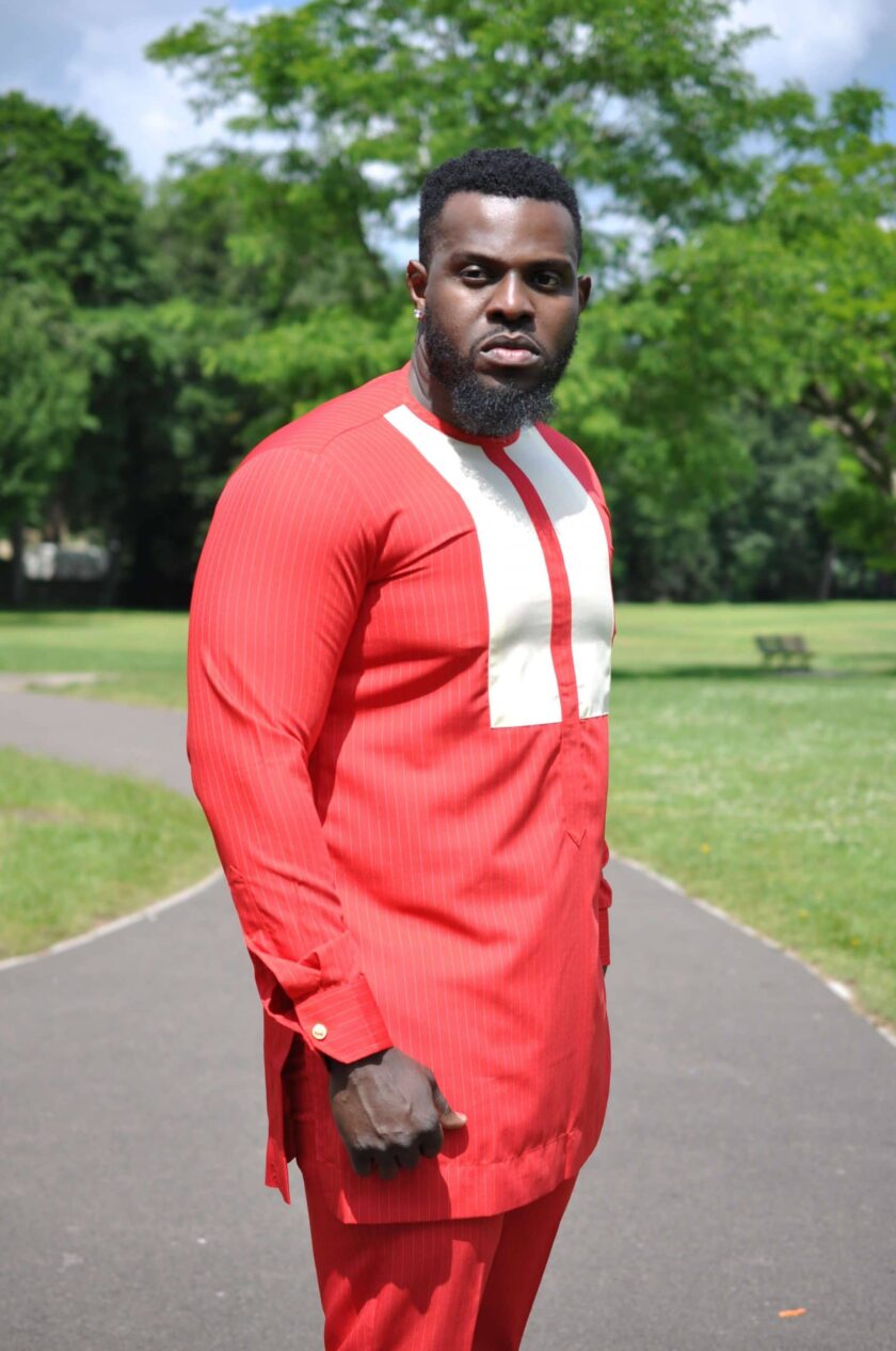Close side shot of model wearing a solid red custom made African suit top with a round neckline and white embroidery detail on the chest.