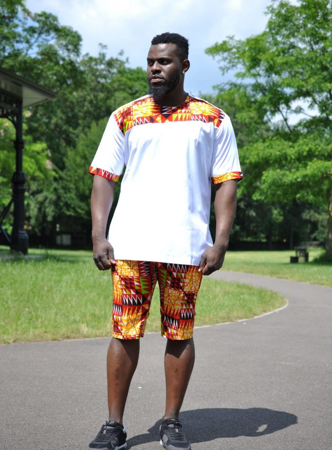 White & African Print Short Pants Matching Set / Co-ord from African Clothing Store. SKU: 19256. White short sleeved shirt with round neckline. .Featuring orange and yellow, multi-coloured African print on a banner across the upper chest and sleeve hem. Comes as a matching set, short pants set or two piece set. The shorts are in the same multi-coloured African print to match the top..