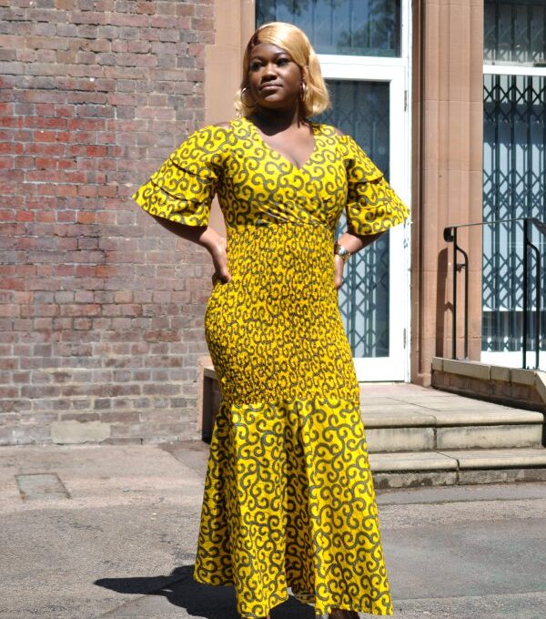 Full frontal of model wearing a full length bodycon flare dress in all over African print.