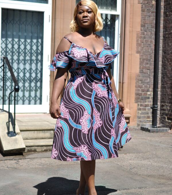 Full frontal of model wearing a cold shoulder wrap front midi dress in colourful swirly African print. Base colour ispurple / brown with splashes of blue and pink.