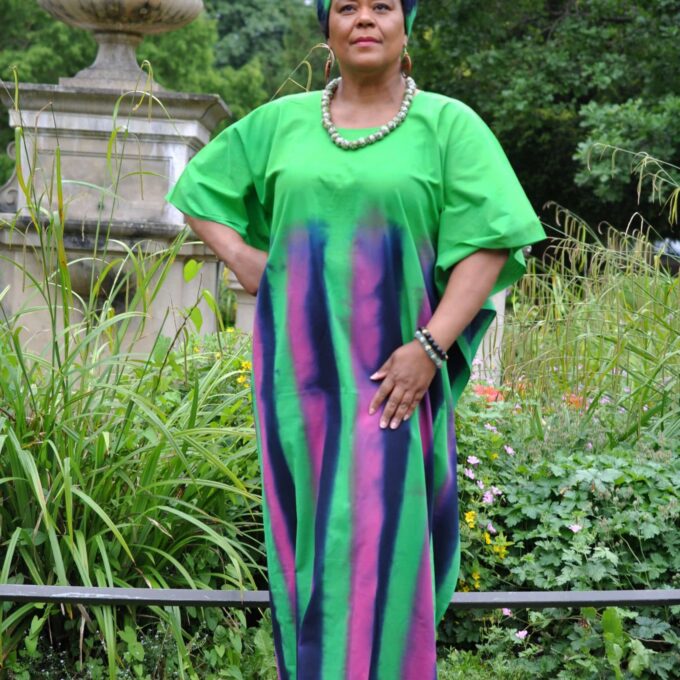 Full frontal of model wearing a long green kaftan dress with pink and blue vertical stripes from chest downwards.