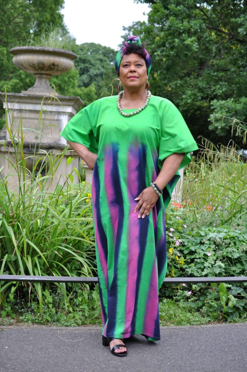 Full frontal of model wearing a long green kaftan dress with pink and blue vertical stripes from chest downwards.