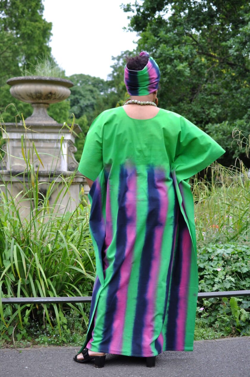 Back shot of model wearing a long green kaftan dress with pink and blue vertical stripes from mid-back downwards.