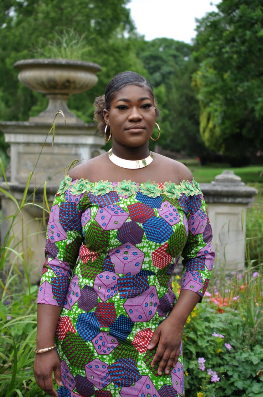 Close front shot of model wearing a colourful lace trim African print fit and flare dress with all over colourful cube and dice print.