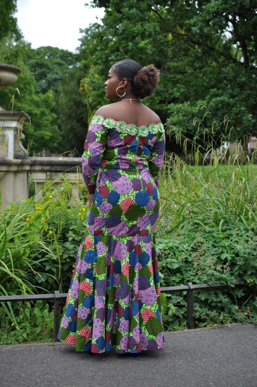 Back shot of model wearing a colourful fit and flare occasion dress with lace trim on the neckline and with flare from mid-thigh.