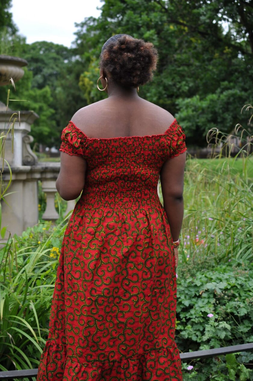 Back shot of model wearing a cap sleeve red and gold African print maxi dress.