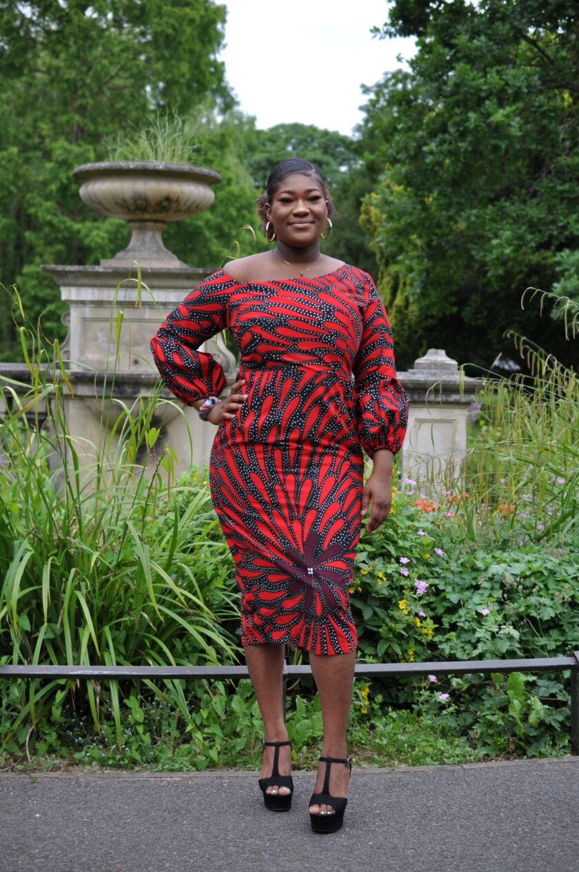 Full frontal of model wearing a custom made long sleeved red and black bodycon midi dress in all over African print.