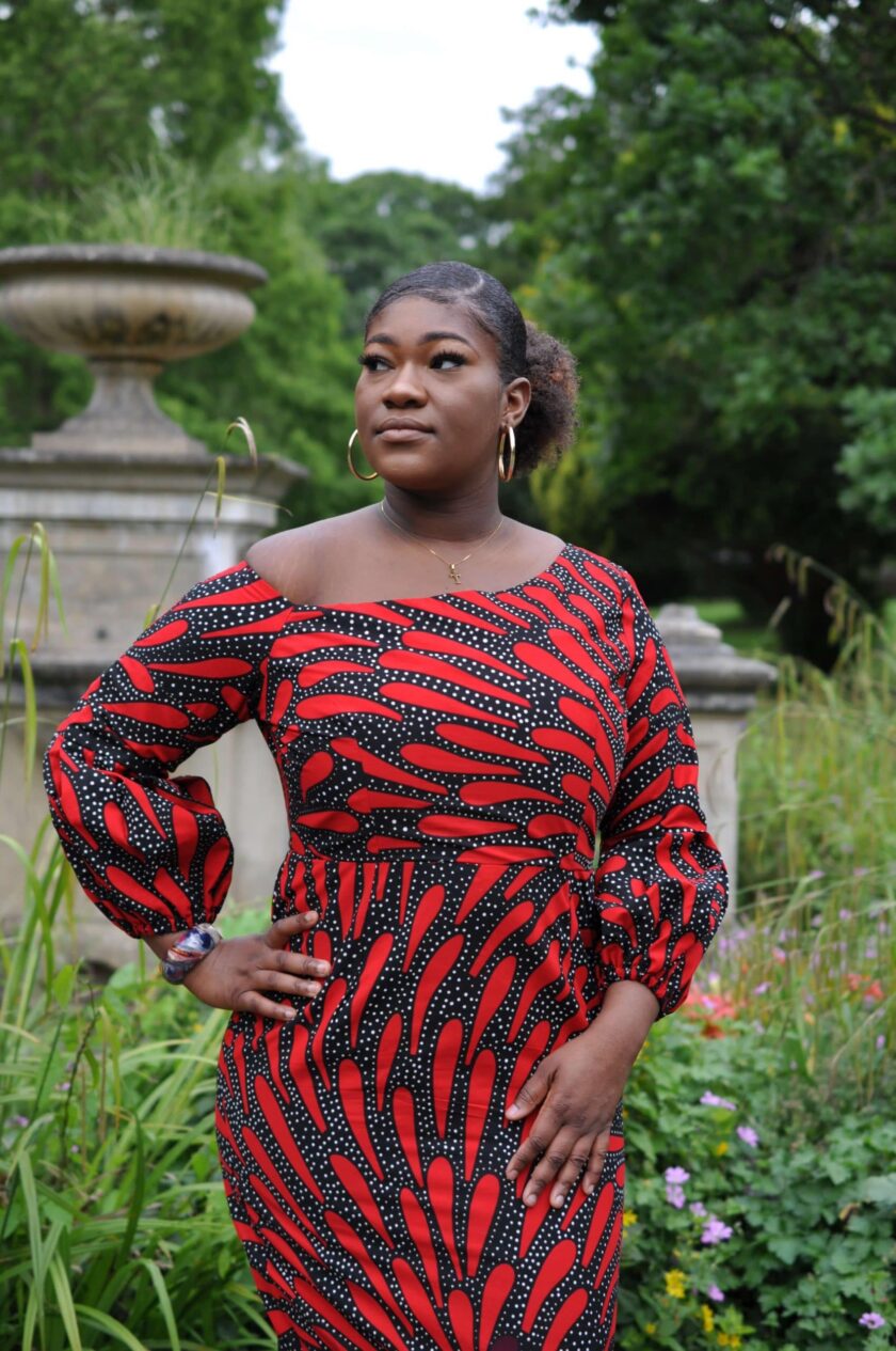 Close up of model wearing scoop neck red and black bodycon midi dress in all over African print