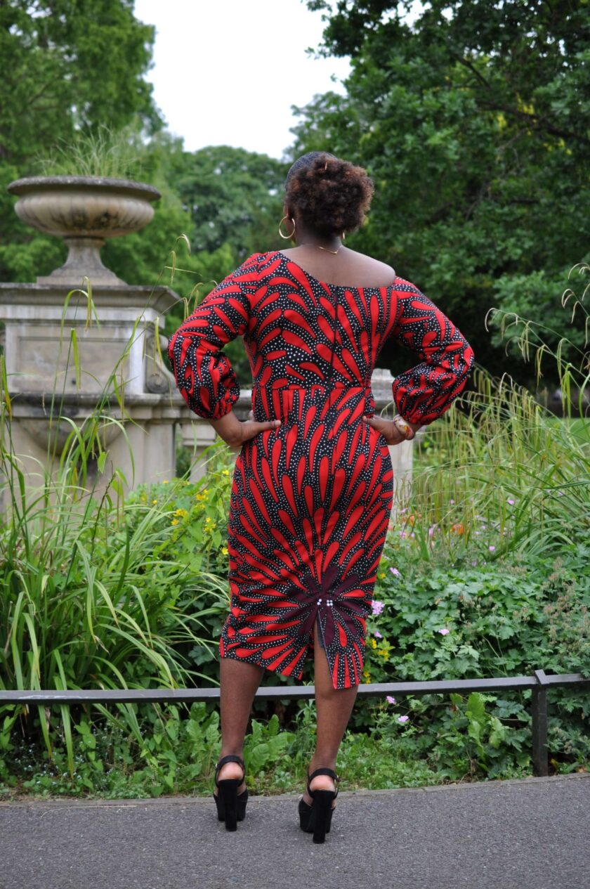 Back shot of model wearing a red and black bodycon midi dress with slit at the rear.