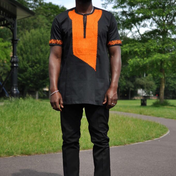 Frontal of model wearing a traditional African black shirt with vibrant orange embroidery.