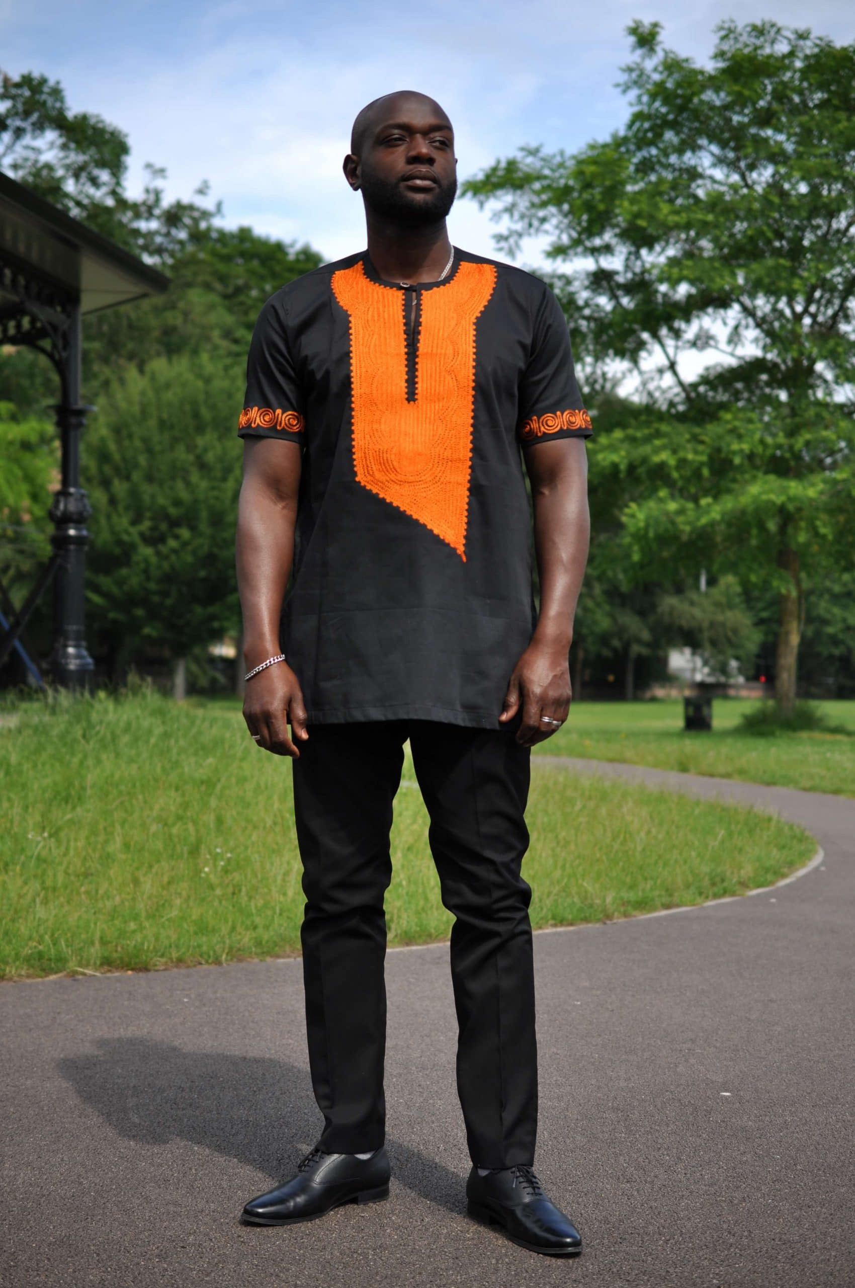 Frontal of model wearing a traditional African black shirt with vibrant orange embroidery.