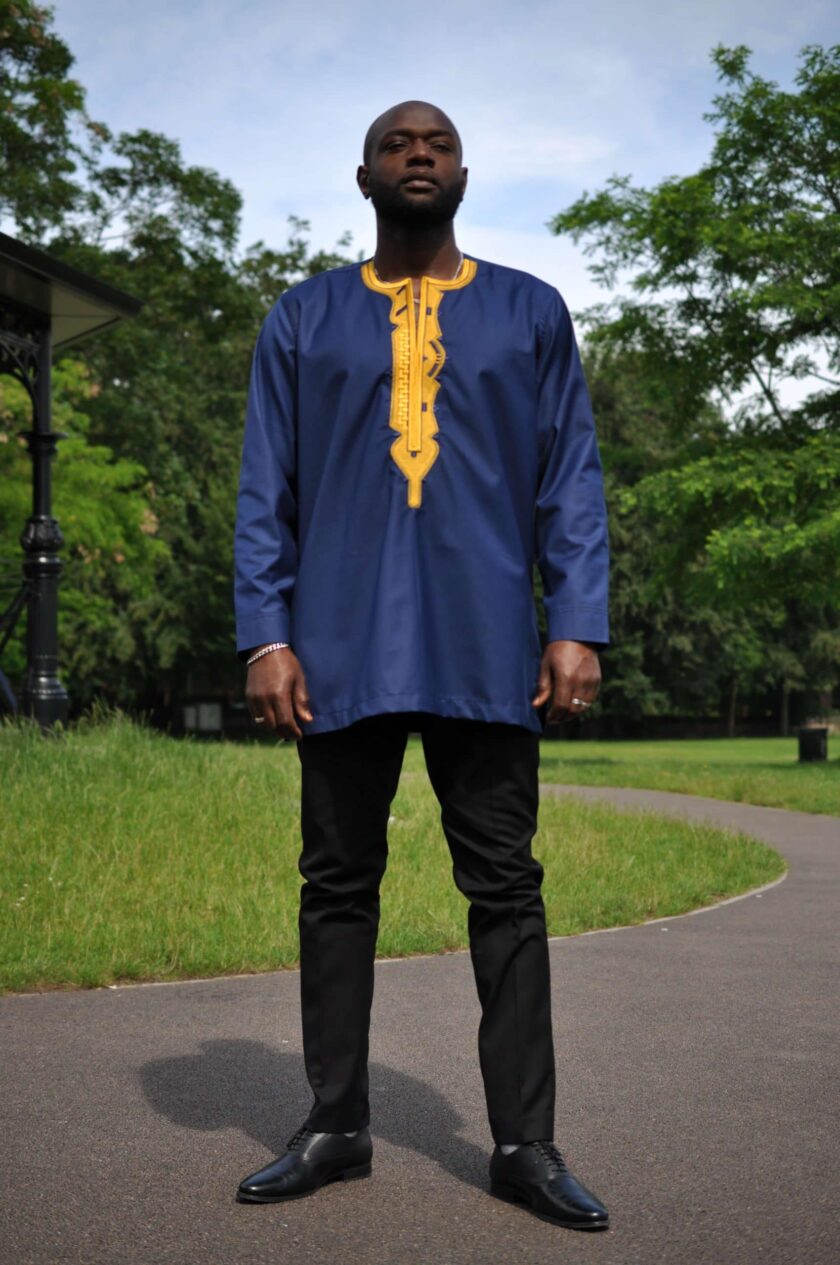 Frontal of model wearing a navy blue traditional African shirt with bright gold embroidery.