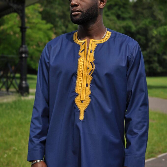 Frontal of model wearing a navy blue traditional African shirt with bright gold embroidery.