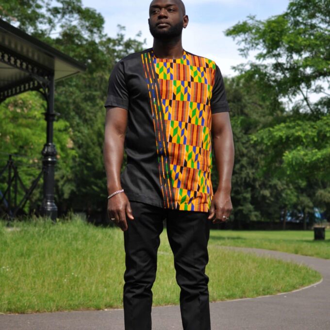 Full frontal of model wearing a solid black short sleeve shirt with African Kente print on front left of shirt.
