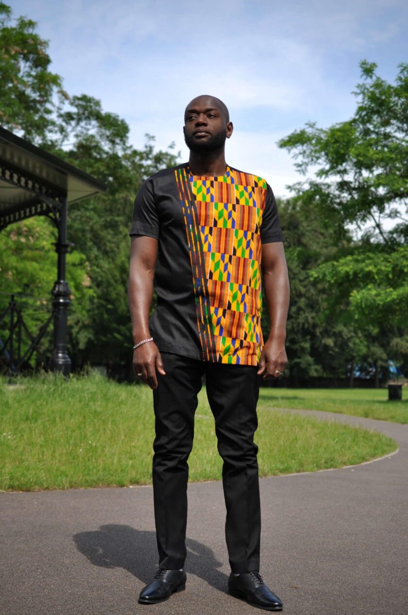 Full frontal of model wearing a solid black short sleeve shirt with African Kente print on front left of shirt.