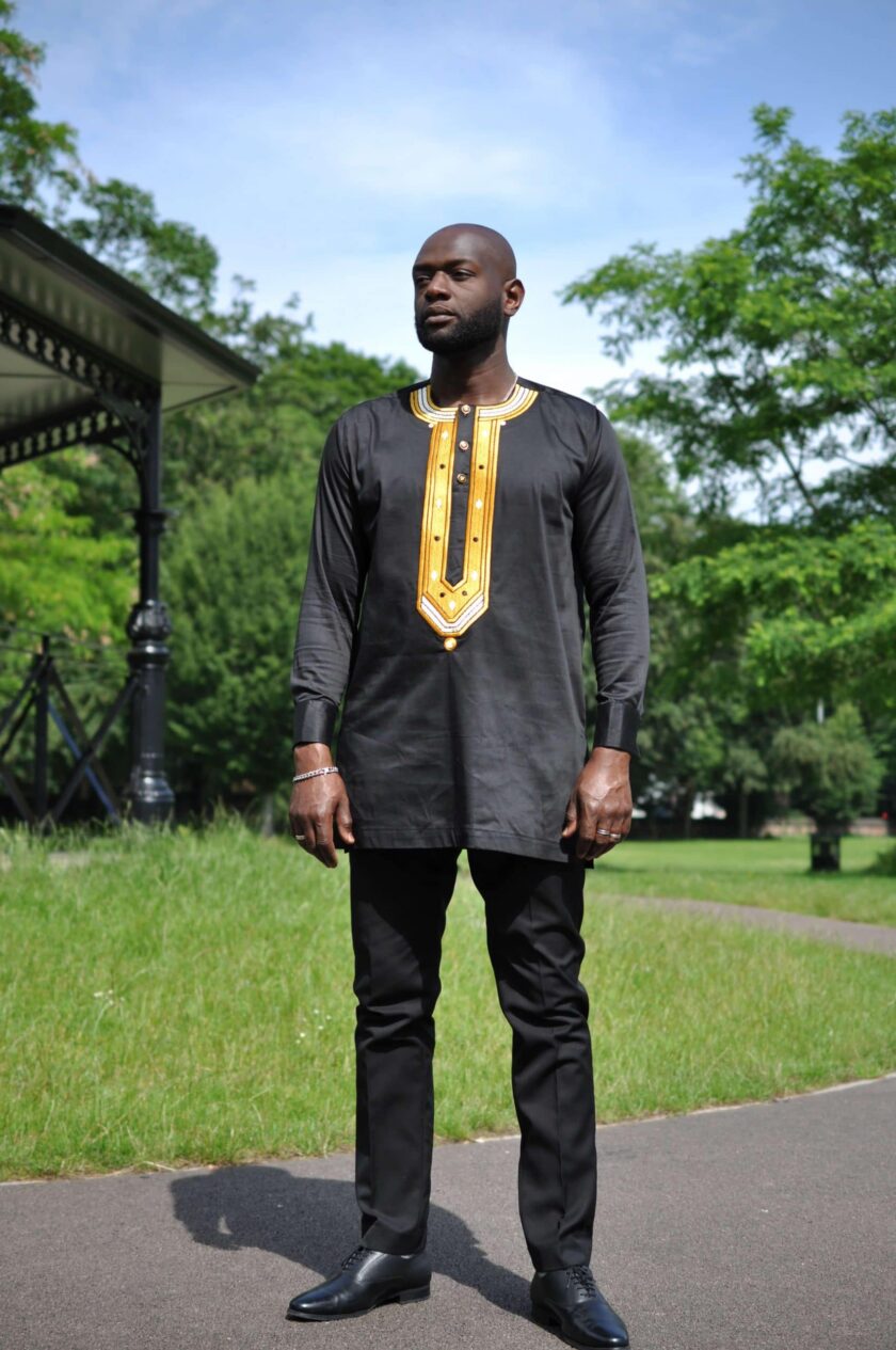 Full frontal of model wearing a solid black men's African shirt with a gold embroidery panel on the chest.