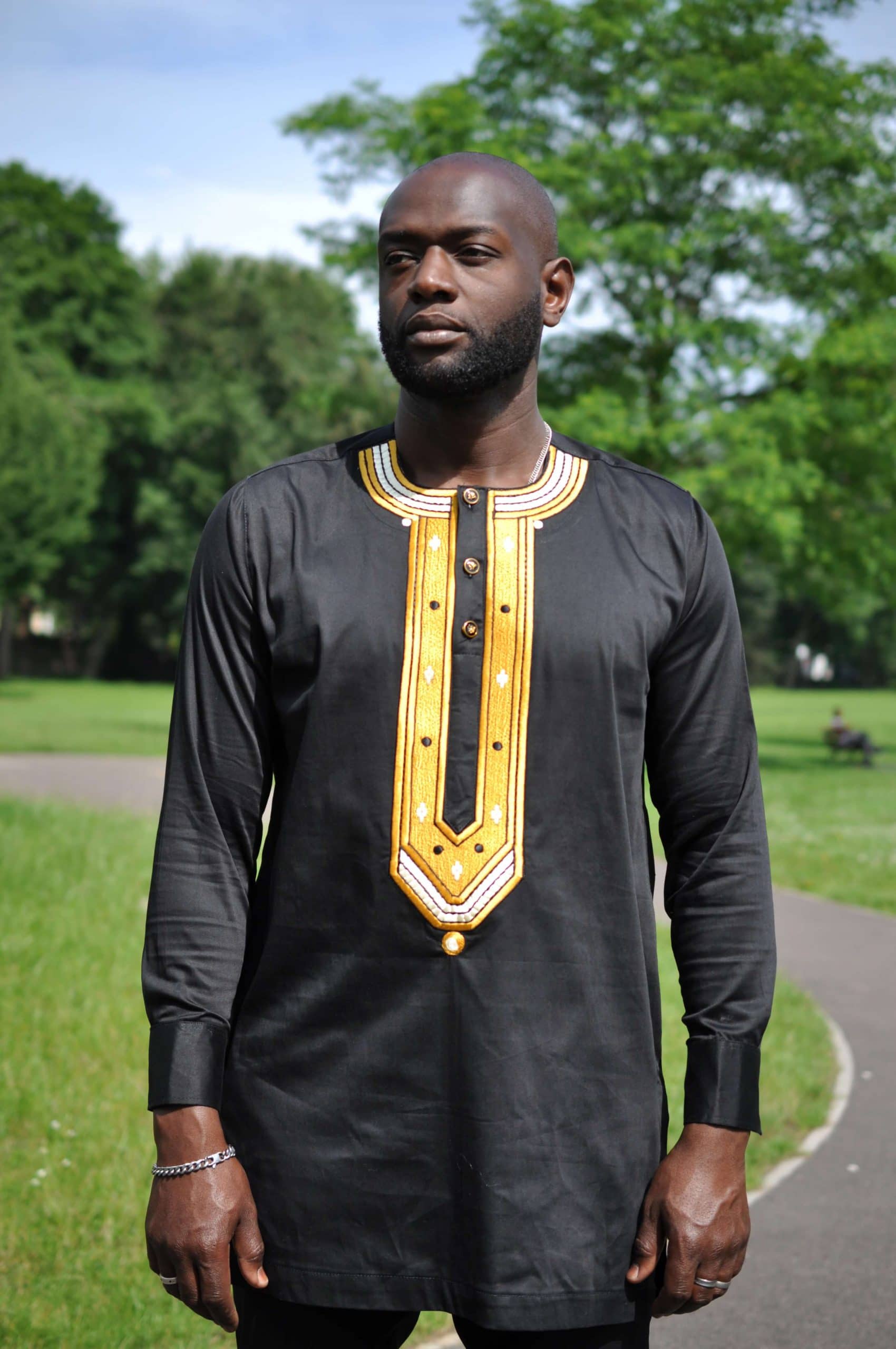 Close frontal of model wearing a solid black men's traditional African shirt with a gold embroidery panel on the chest.