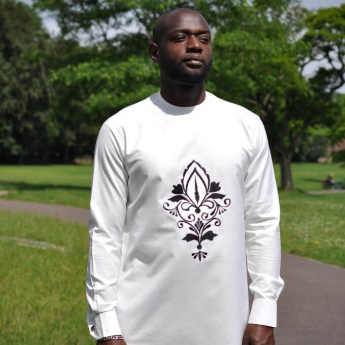 Close front shot of model wearing a solid cream men's African suit top with a printed flower image on the chest.