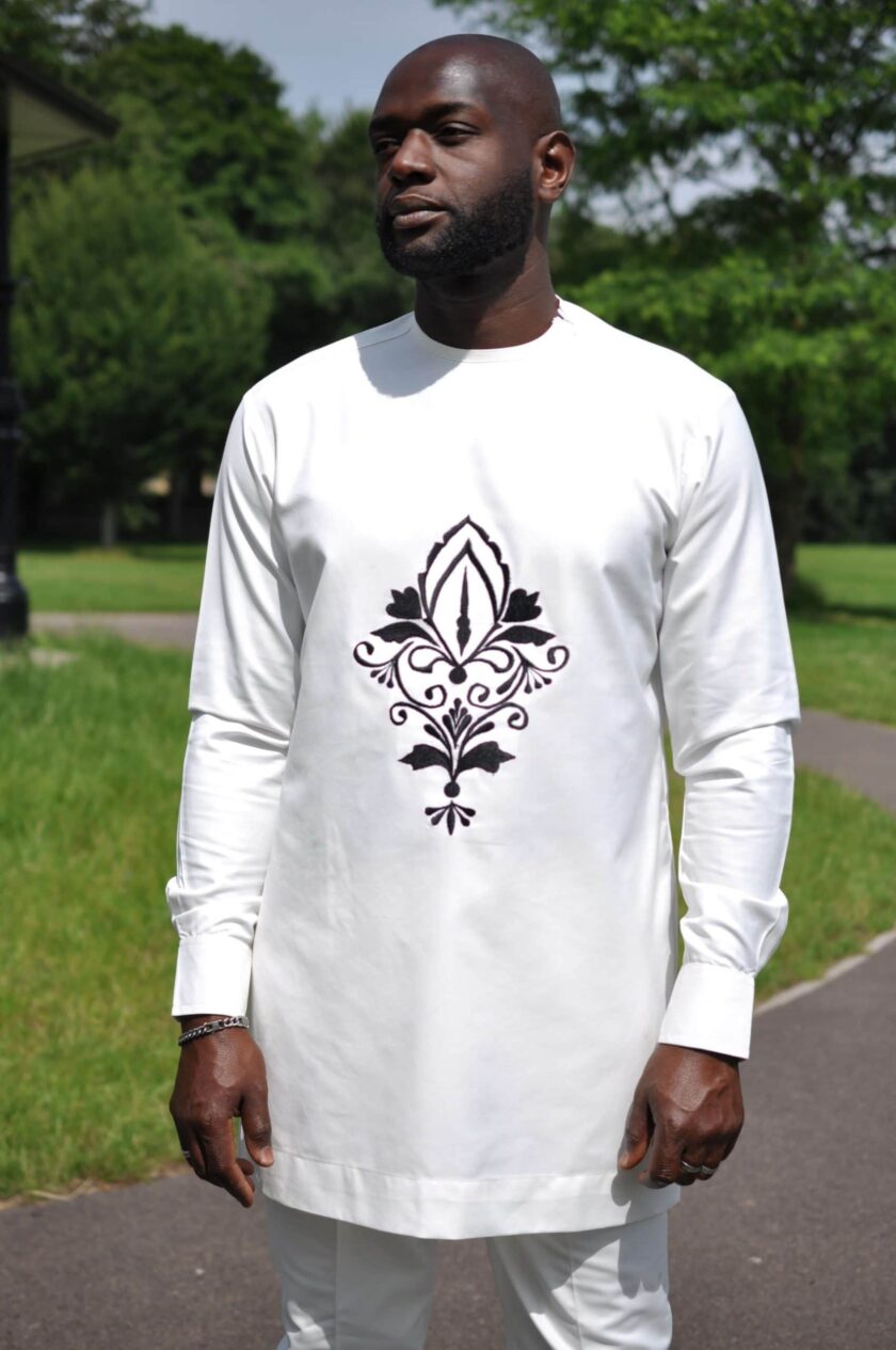 Close frontal of model wearing a solid cream men's African suit with a dark flower print image on the front.