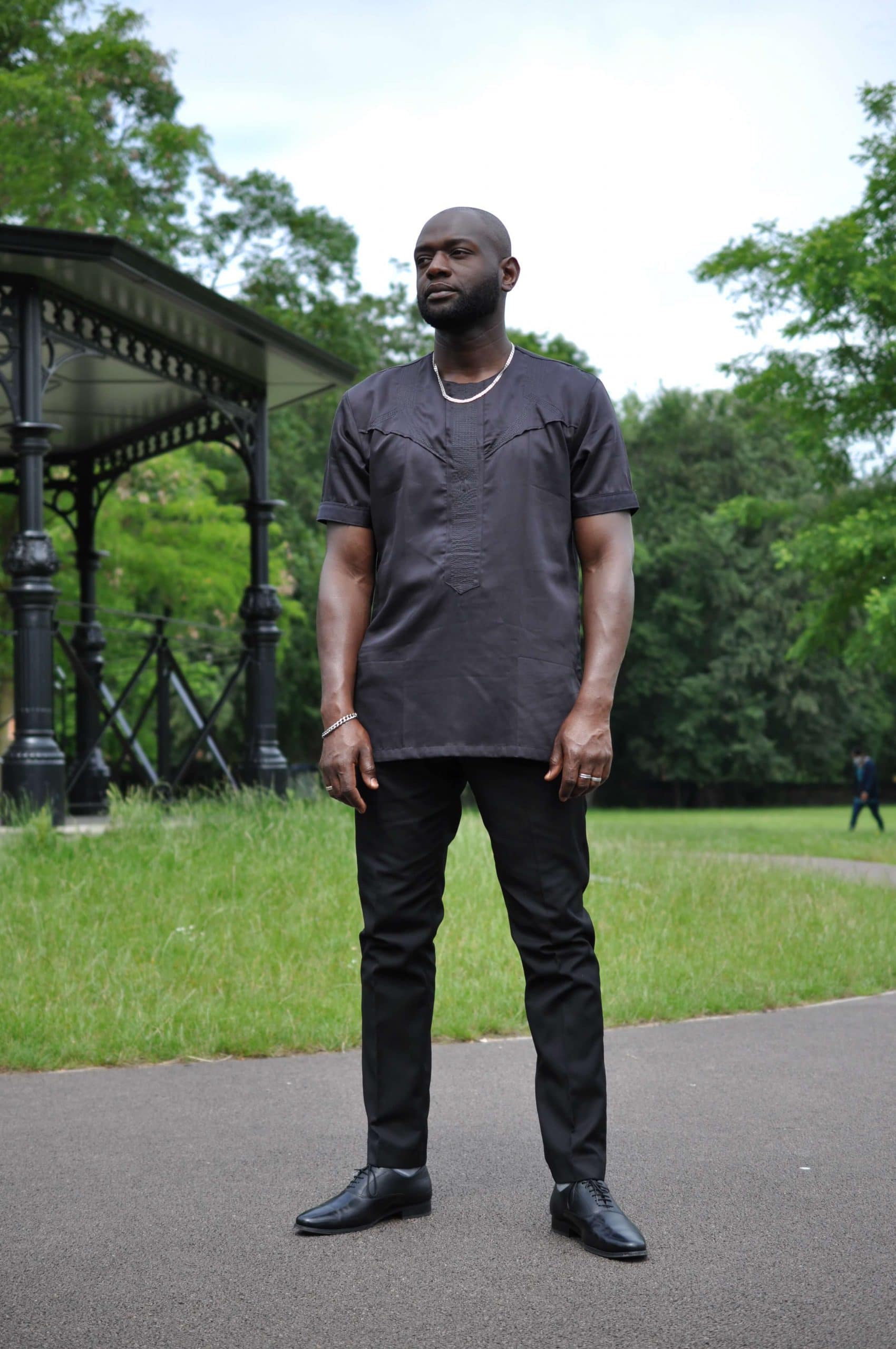 Full frontal of model wearing a solid black short sleeve African shirt with a simple embroidery design on the chest.