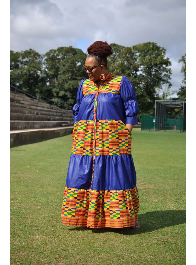 Frontal of model wearing a long blue and Kente print smock dress with stand collar and lantern sleeves.