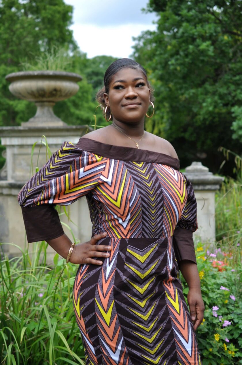 Frontal of model wearing a multi-coloured off shoulder midi dress in all over African print.