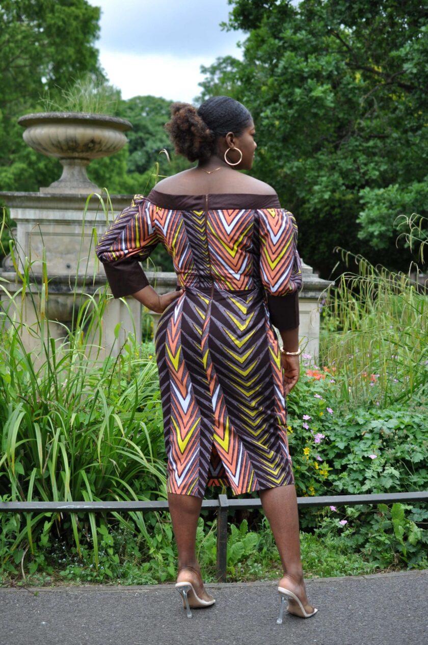 Back shot of model wearing a multi-coloured off shoulder midi dress in all over African print.