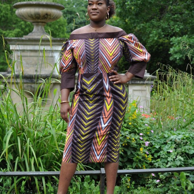 Frontal of model wearing a multi-coloured off shoulder midi dress in all over African print.
