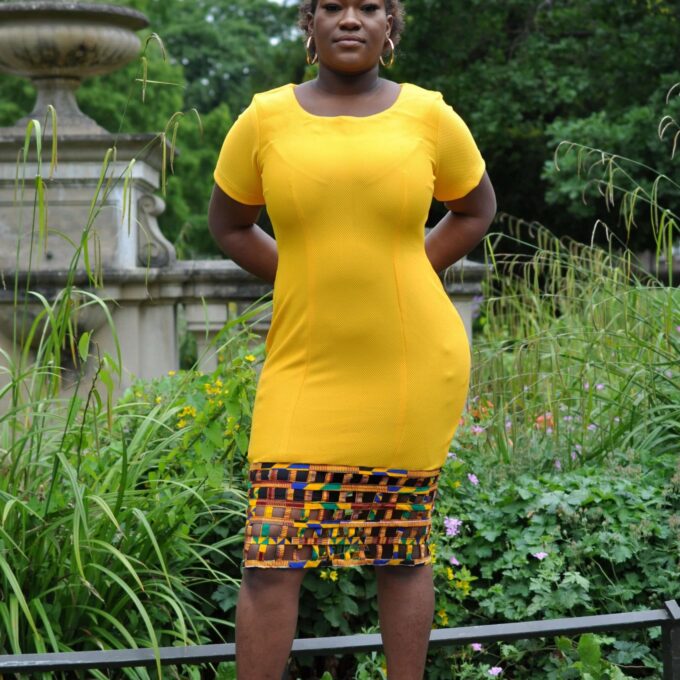 Full frontal of model wearing a solid yellow short sleeve bodycon midi dress with African Ankara print mesh hem.