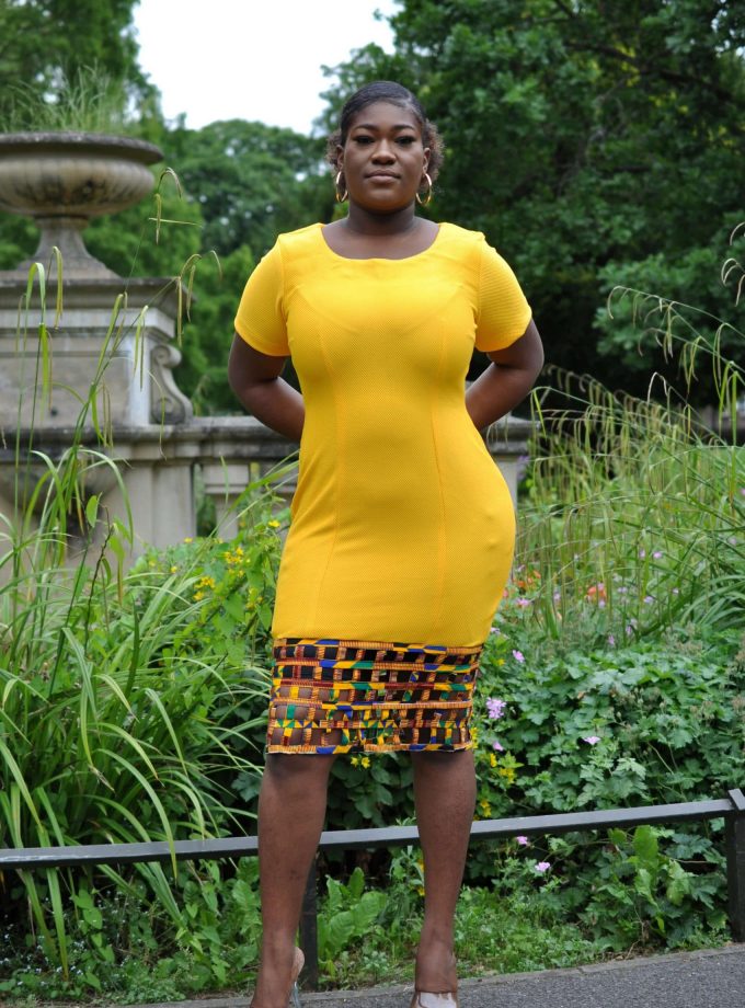 Full frontal of model wearing a solid yellow short sleeve bodycon midi dress with African Ankara print mesh hem.