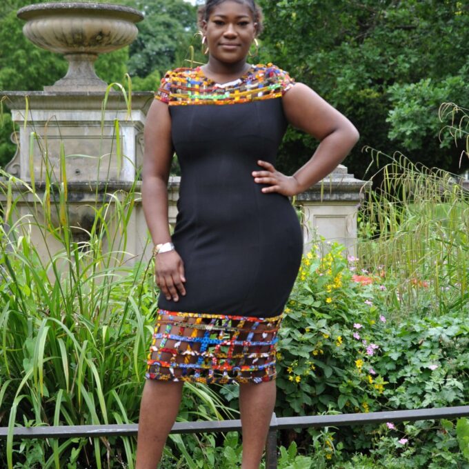 Full frontal of model wearing a solid black bodycon dress with mesh detail on the neckline and hem in multi-coloured African print.