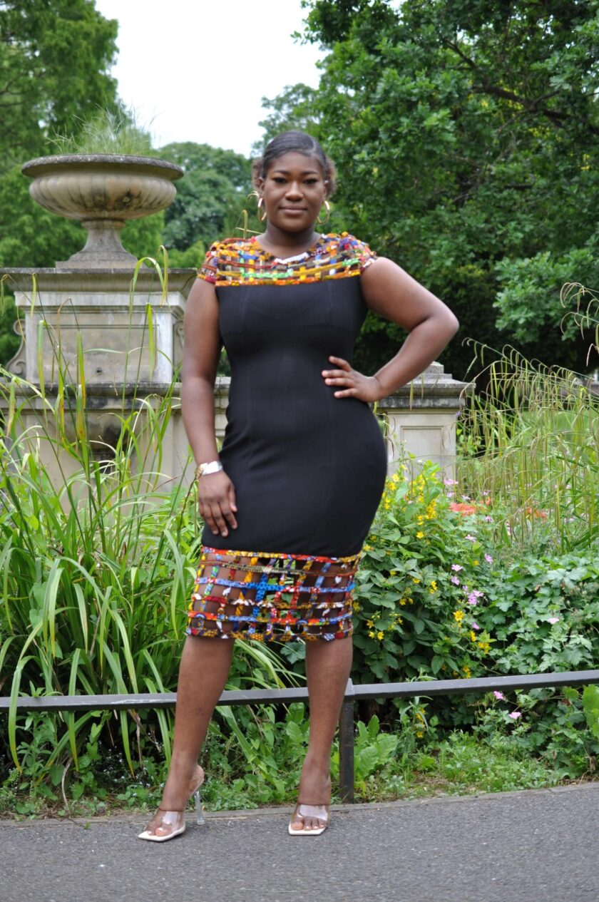 Full frontal of model wearing a solid black bodycon dress with mesh detail on the neckline and hem in multi-coloured African print.