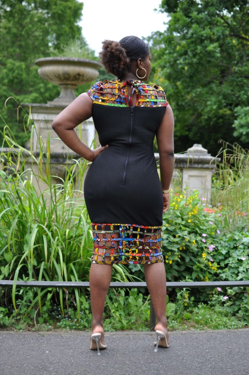 Back shot of model wearing a black bodycon dress with African print mesh detail.