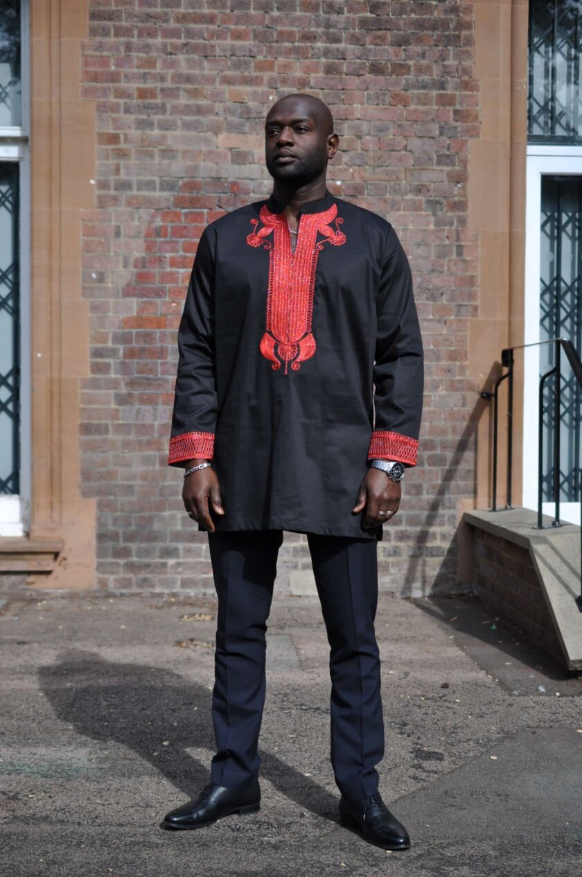 Frontal of model wearing a men's black African suit with stunning red embroidery on neckline, chest, cuffs and rear neckline.