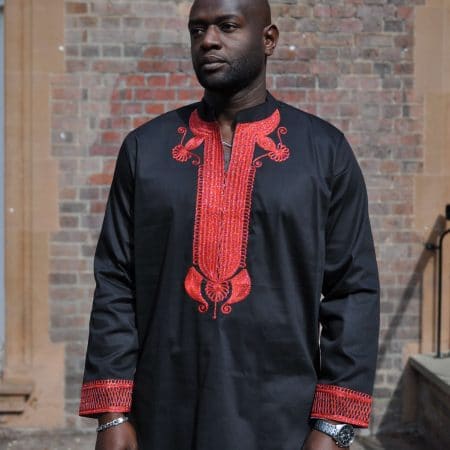 Frontal of model wearing a men's black African suit with stunning red embroidery on neckline, chest, cuffs and rear neckline.