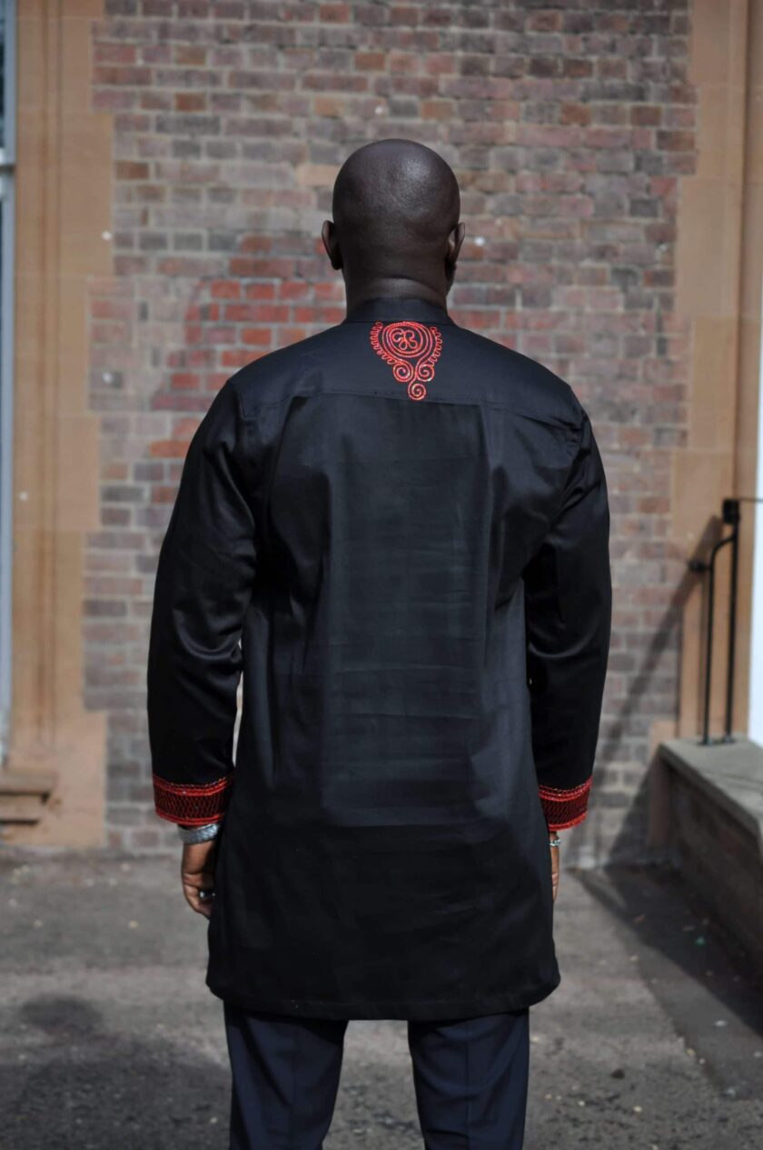 Frontal of model wearing a men's black African suit with stunning red embroidery on neckline, chest, cuffs and rear neckline.