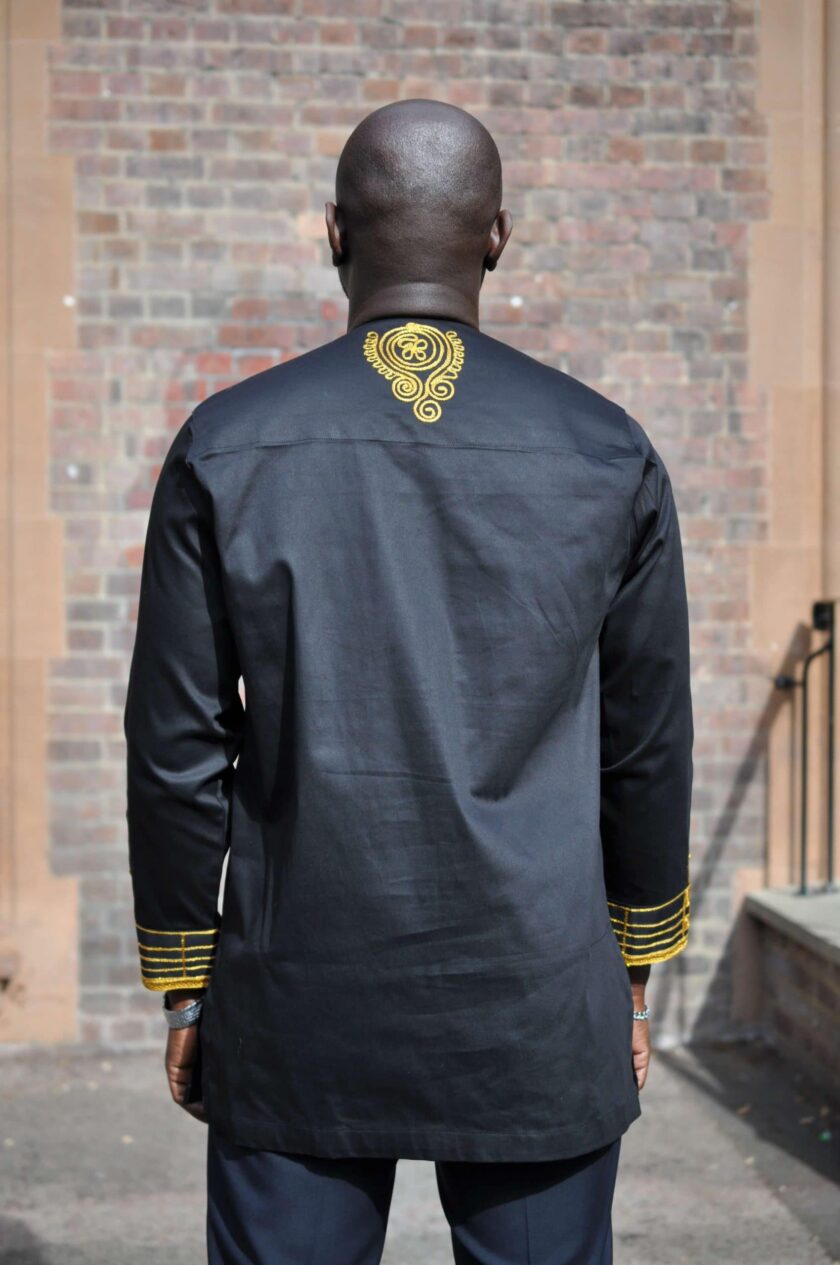 Back shot of model wearing a men's traditional African black shirt with gold embroidery on the back neckline and cuffs.