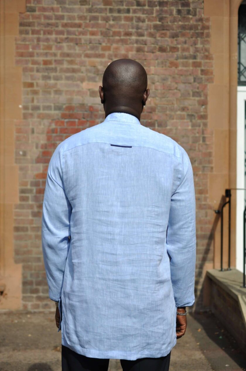 Back shot of model wearing a light blue men's long sleeve polo shirt made from linen. Features a piece of navy blue trim on upper back.