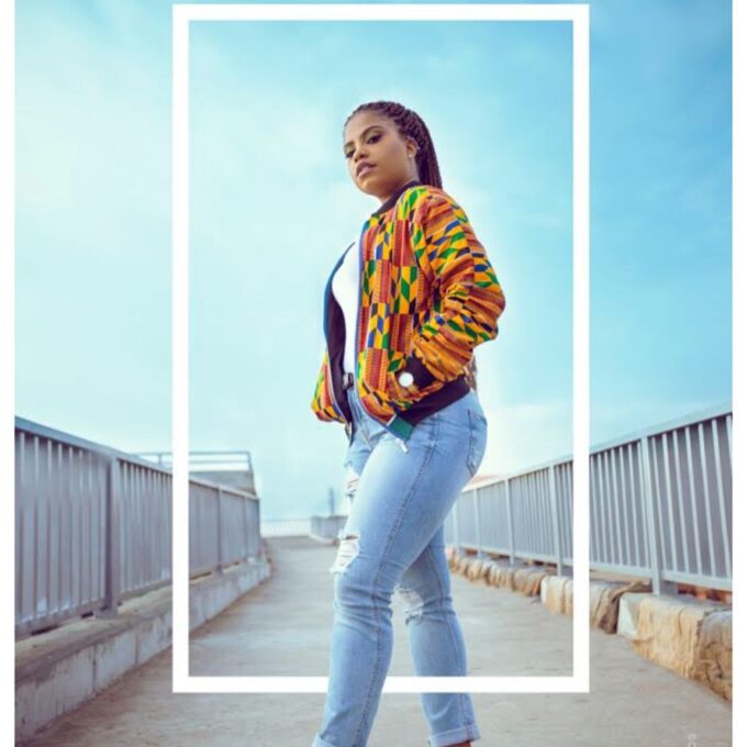 Frontal of model wearing our ladies Deja African inspired bomber jacket in all over vibrant multi-coloured African Kente print pattern. Features a black baseball collar.