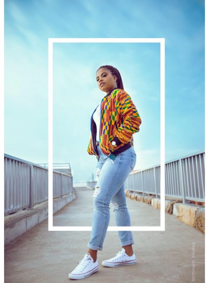 Frontal of model wearing an African inspired unisex bomber jacket in all over vibrant multi-coloured African Kente print.